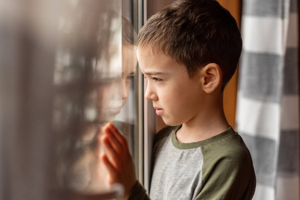 The boy looks out the window and wants to go out for a walk. But he stays at home. Close-up. Quarantine. - Фото, зображення
