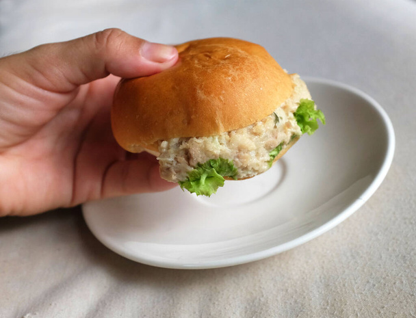 woman hand holding mini Tuna burger with mayonnaise on a white plate. Delicious breakfas. - Photo, Image
