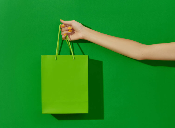 女性の手は緑の背景にショッピングバッグを保持。ショッピングのコンセプト - 写真・画像