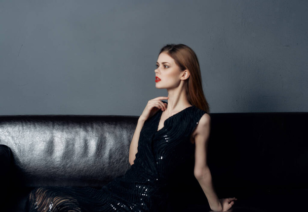 美しい女性で黒のドレスに座ってソファの上にポーズインテリアグラマー - 写真・画像
