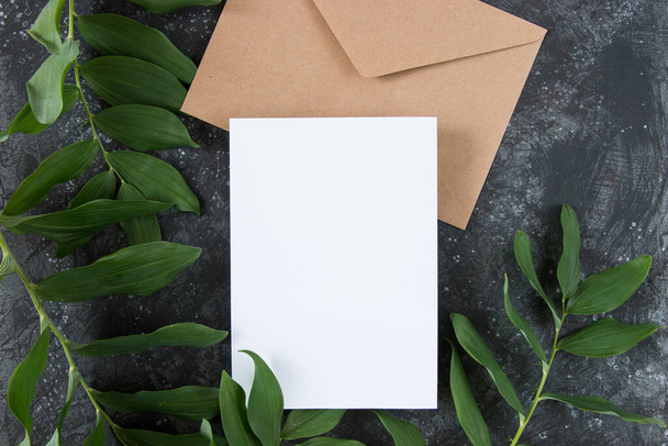 Plaats van uitnodiging lay-out met bladeren. Blanco wenskaarten, een envelop en een blanco vel papier op een donkere achtergrond. Vrouwelijk stilleven. Vlakke lay, bovenaanzicht - Foto, afbeelding