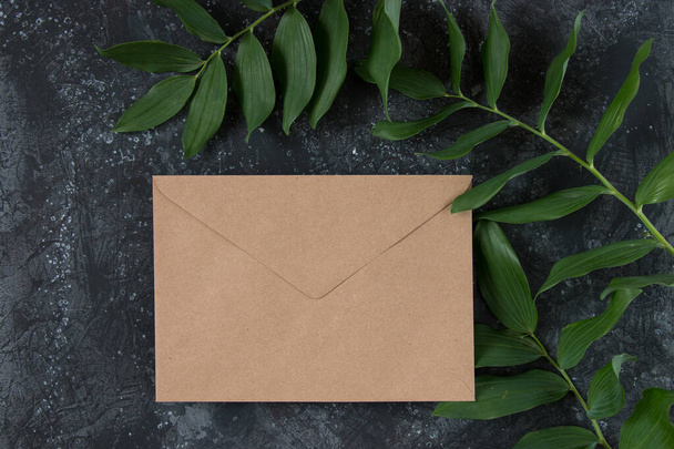Scène de mise en page d'invitation avec feuilles. Cartes de vœux vierges, une enveloppe et une feuille de papier vierge sur fond sombre. Femme nature morte. Couché plat, vue du dessus - Photo, image