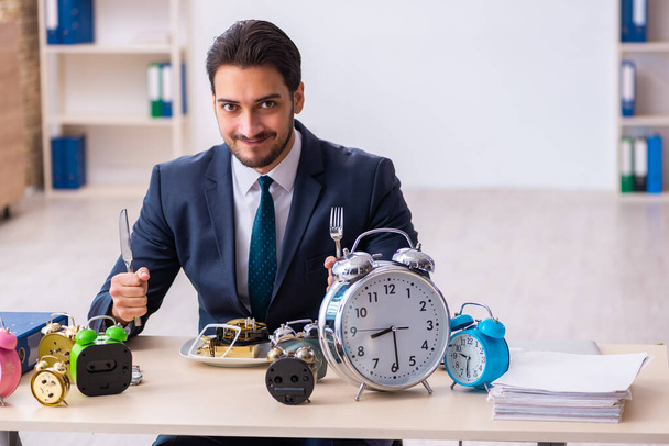 Joven empleado de negocios comiendo despertador-reloj - Foto, Imagen