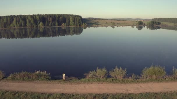 Hombre pescando en muelle de madera cerca del lago - Imágenes, Vídeo