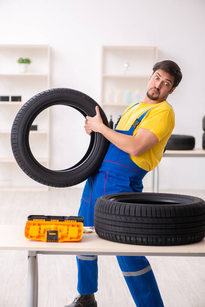 Joven trabajador de garaje con neumático en el taller - Foto, imagen