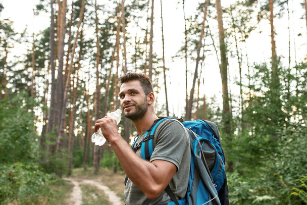 Happy young caucasian man drinking water while trekking - Photo, image