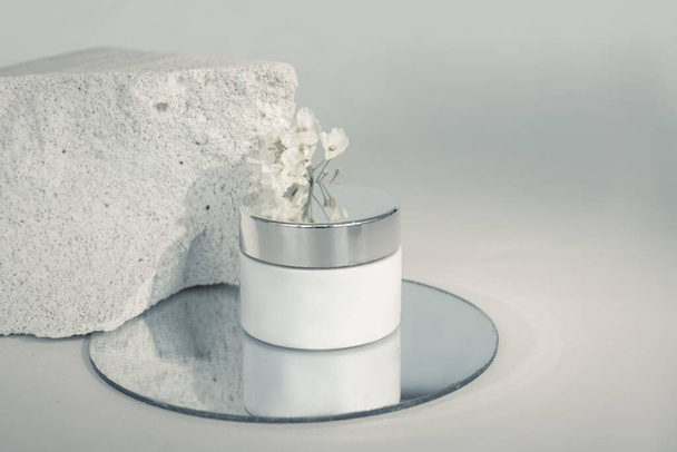 cream box on piece of concrete in cut. Porous structure of concrete is associated with texture of human skin. Composition uses amirror and delicate flower. Medical cosmetics concept - Photo, Image