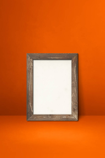 Wooden picture frame leaning on an orange wall. Blank mockup template - Fotó, kép