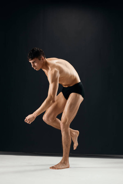 athletic men muscular body in black panties bent leg dark background - Foto, imagen