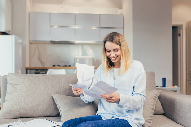 Happy blonde woman sitting at home on the couch, happy with timely payment of credit bills and closing the credit line, received good news from the bank - Fotoğraf, Görsel