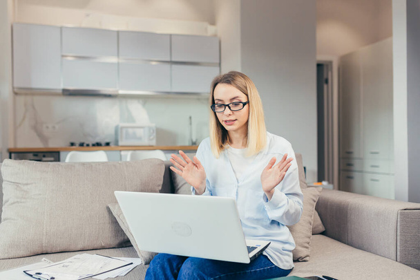 Beautiful woman holds online consultation using laptop sitting on sofa at home - Foto, Bild
