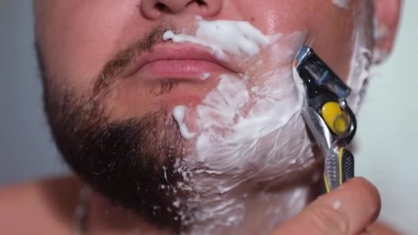 Een man scheert zijn gezicht met een scherp lemmet.. - Video