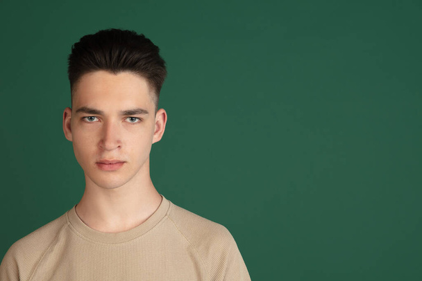 Portrait of young Caucasian boy isolated on green studio background. Concept of facial expressions, human emotions. - Fotó, kép