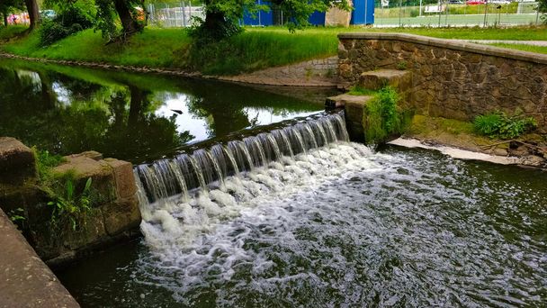 Tiny weir on a small rivulet going through one of the Prague's park. The water makes white riffles on the edge of the weir. - Photo, Image