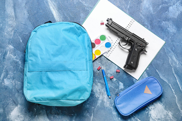 Пистолет и рюкзак с канцелярскими принадлежностями на цветном фоне. Концепция стрельбы в школе - Фото, изображение