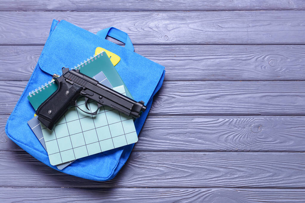 Pistolet i plecak z notatnikami na drewnianym tle. Koncepcja strzelania do szkół - Zdjęcie, obraz