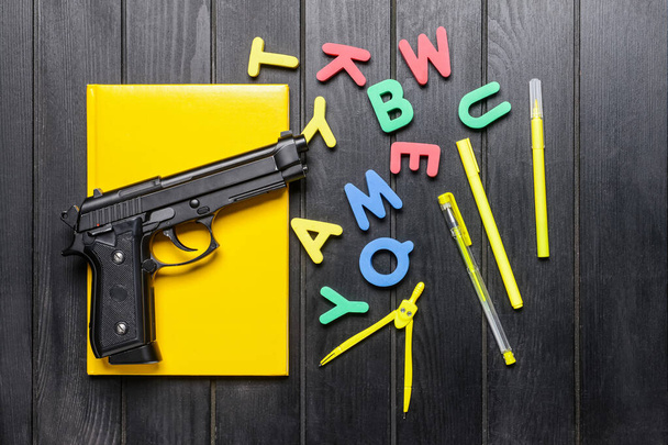 Pistola e artigos de papelaria sobre fundo de madeira escura. Conceito de tiroteio escolar - Foto, Imagem