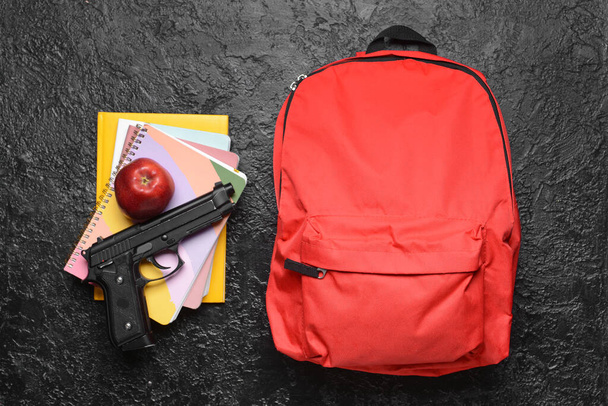 Pistola e mochila com papelaria sobre fundo escuro. Conceito de tiroteio escolar - Foto, Imagem