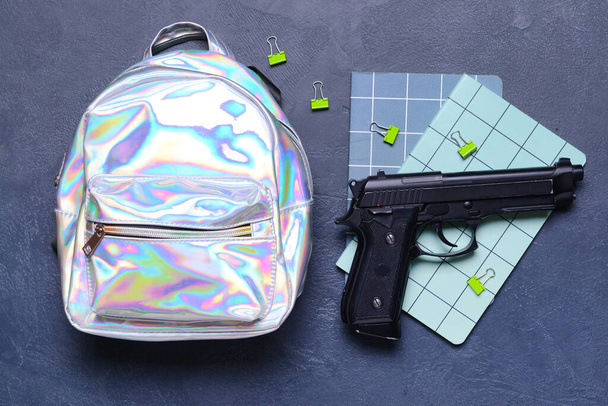 Pistola e mochila com papelaria sobre fundo escuro. Conceito de tiroteio escolar - Foto, Imagem