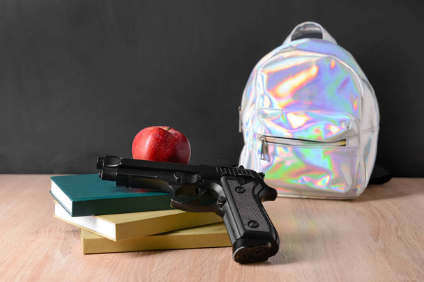 Пистолет с книгами и рюкзаком на столе в классе. Концепция стрельбы в школе - Фото, изображение