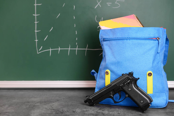 Pistol and backpack on table in classroom. Concept of school shooting - Photo, Image