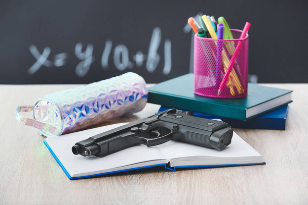 Pistol and stationery on table in classroom. Concept of school shooting - Photo, Image