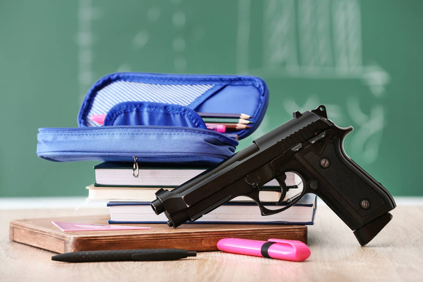 Pistol and stationery on table in classroom. Concept of school shooting - Foto, afbeelding