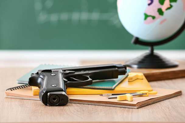 Sınıftaki masa, tabanca ve kırtasiye malzemesi. Okul çatışması kavramı - Fotoğraf, Görsel