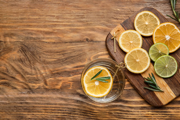 Glass of healthy lemonade and citrus fruits on wooden background - Foto, afbeelding