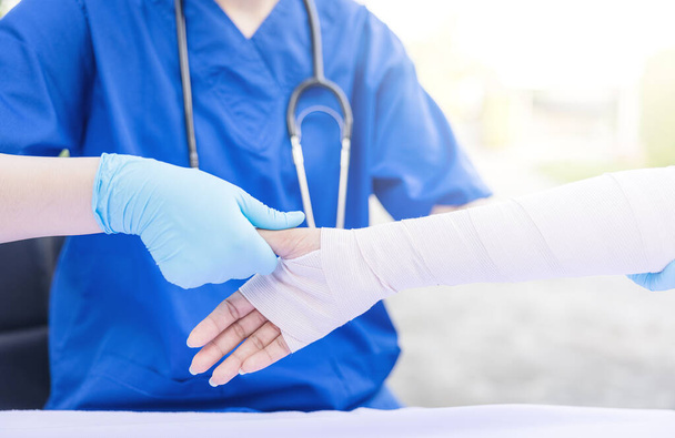 Close-up de médico feminino colocando uma bandagem no membro superior da mão lesionada do paciente. - Foto, Imagem