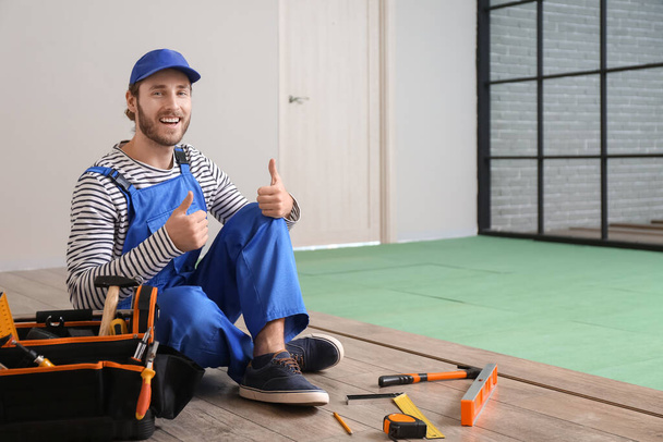 Carpenter showing thumb-up during installing of laminate flooring in room - Foto, Imagen