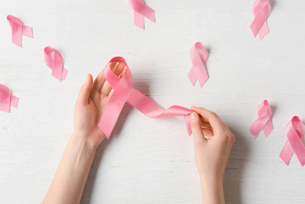 Жіночі руки з рожевими стрічками на світлому дерев'яному тлі. Концепція раку молочної залози
 - Фото, зображення