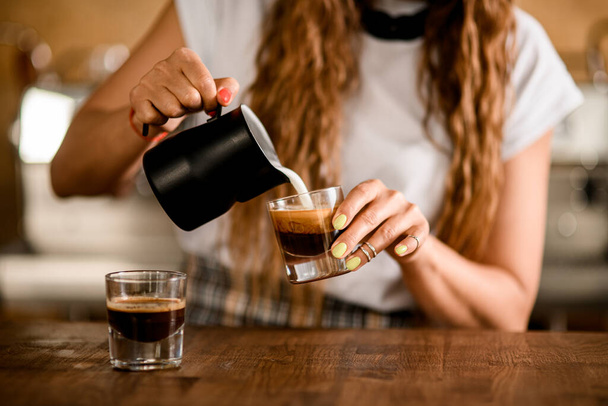 close-up on glass with coffee drink in which woman barista pours milk - Foto, imagen