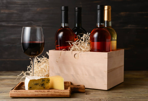 Box with bottles of wine, cheese and glass on dark wooden background - Photo, Image