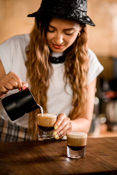 woman barista accurate pours whipped milk cream in glass with coffee drink - Фото, зображення