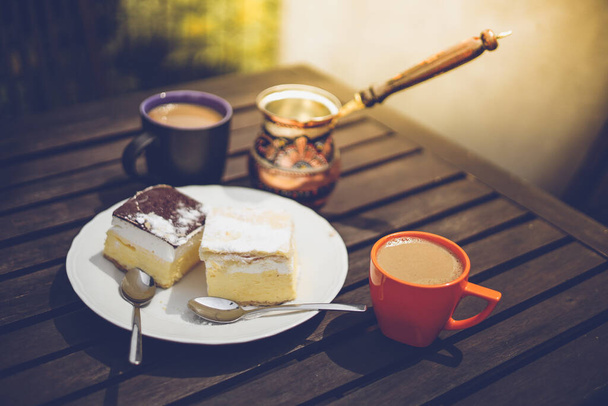 Rustic breakfast. Wooden coffee table with coffee cups, cezve, lake Bled cream cake, delicious slovenian dessert. Kremna Rezina or Cremeschnitte - Fotó, kép