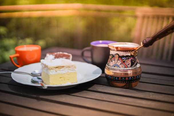 Maalaismainen aamiainen. Puinen sohvapöytä kahvikupeilla, cezve, järvi Bled kerma kakku, herkullinen slovenian jälkiruoka. Kremna Rezina tai Cremeschnitte - Valokuva, kuva