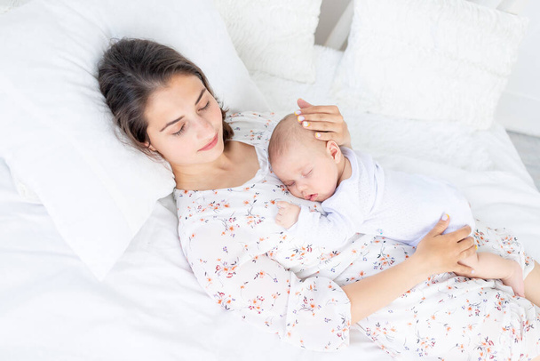 mom and newborn baby sleep together, mom puts baby to sleep on the bed in the bedroom, the concept of motherhood and healthy sleep - Фото, зображення