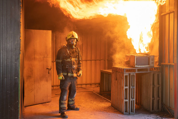 Strażak lub strażak w mundurze używający węża przeciwpożarowego przeciwko gorącemu pożarowi i niebezpiecznemu dymowi w pojemniku, ratownikowi awaryjnemu. Ludzie. Bohater - Zdjęcie, obraz