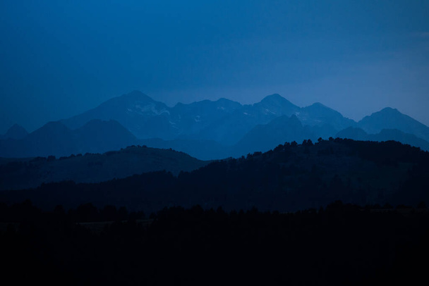 Bergen lagen tijdens het blauwe uur. Landschap met donkerblauwe nevelige silhouetten van alpiene bergen en dennenbossen in de Pyreneeën. - Foto, afbeelding