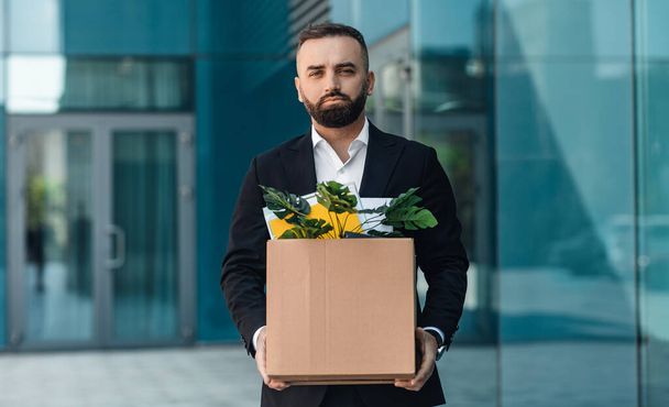 Portrait of fired upset desperate businessman in suit standing outdoors with box of stuff. Male office worker lost job - Foto, Imagen