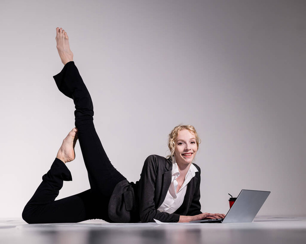 Bailarina descalça vestida em um terno de negócios posa para um laptop e bebe café. Mulher flexível trabalha no computador - Foto, Imagem