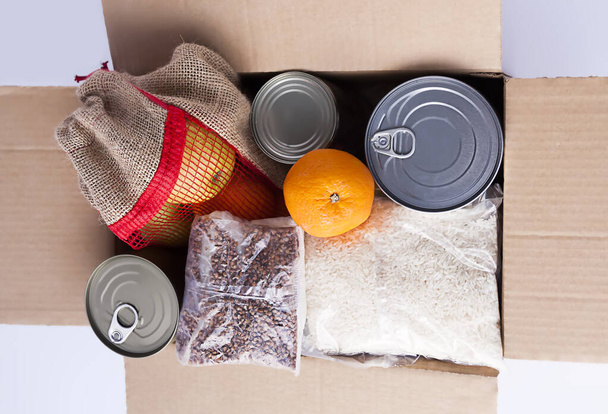 Tin cans, fresh apple fruits, buckwheat and rice packs in a cardboard box. Food donation, delivery theme. - Фото, зображення