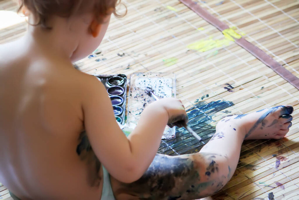 the little girl is sitting on the floor and playing with paints - Foto, imagen