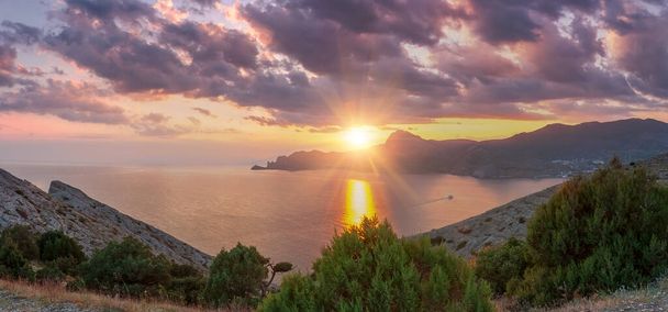 Sudak, Crimea - a view from Cape Meganom. Sunset sky with beautiful clouds. The Black Sea and the ridge of the Crimean mountains in the rays of the evening sun. Panorama. - Foto, Bild