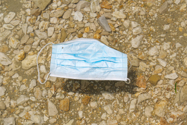 La mascarilla médica azul se encuentra en la playa. Contaminación plástica ambiental y costera durante las pandemias de covid-19 - Foto, Imagen