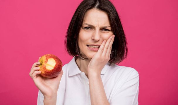 Beautiful young woman bites a big apple and has a toothache - Фото, зображення