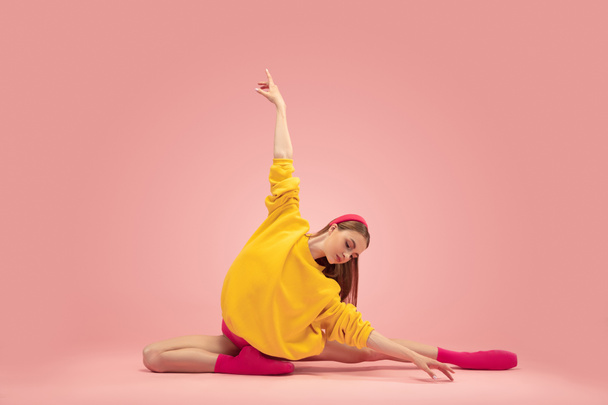 Portrait of young beautiful girl, female ballet dancer training isolated over pink background. - Фото, изображение