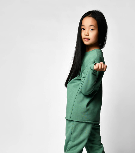 Cute Asian girl with long black hair in a green comfortable suit turns around and looks at you. - Foto, afbeelding