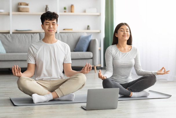 Friedliche asiatische Familie praktiziert Meditation zu Hause mit Laptop - Foto, Bild